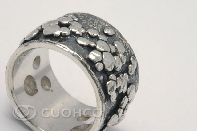 Wide sterling silver ring with gloss particles in relief against a background darkened with patina that suggest the bright wake of a falling star