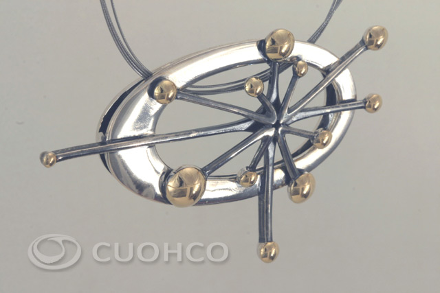 Oval polished silver pendant with a star shaped motif darkened with patina in which gold spheres stand out at the ends
