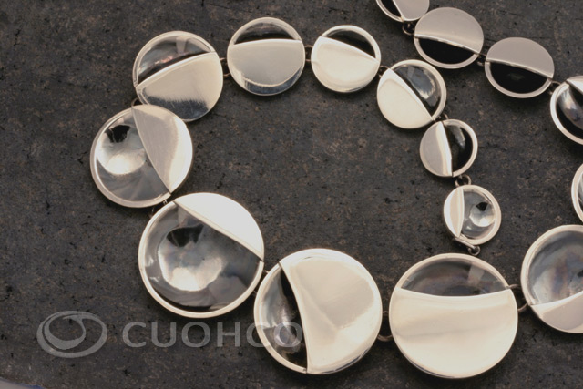 Articulated necklace in solid silver with hemispherical shaped links in progressive decrease in size, each of them partially covered with a silver sheet describing a continuous graceful curve along the necklace