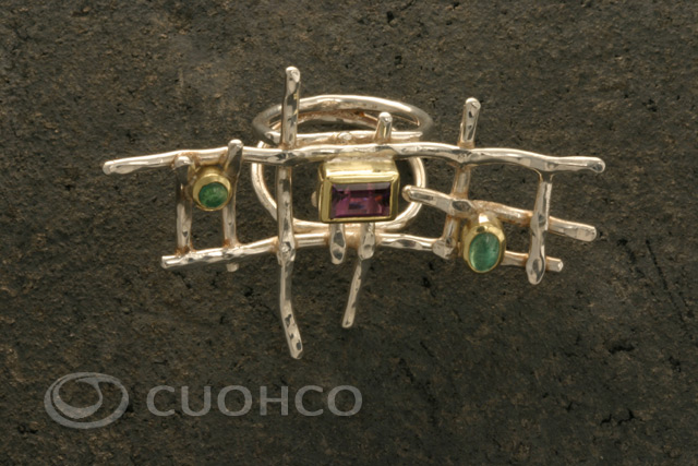 Ring with the shape of an asymmetric silver grid on which are set two emeralds and an amethyst with gold bezels